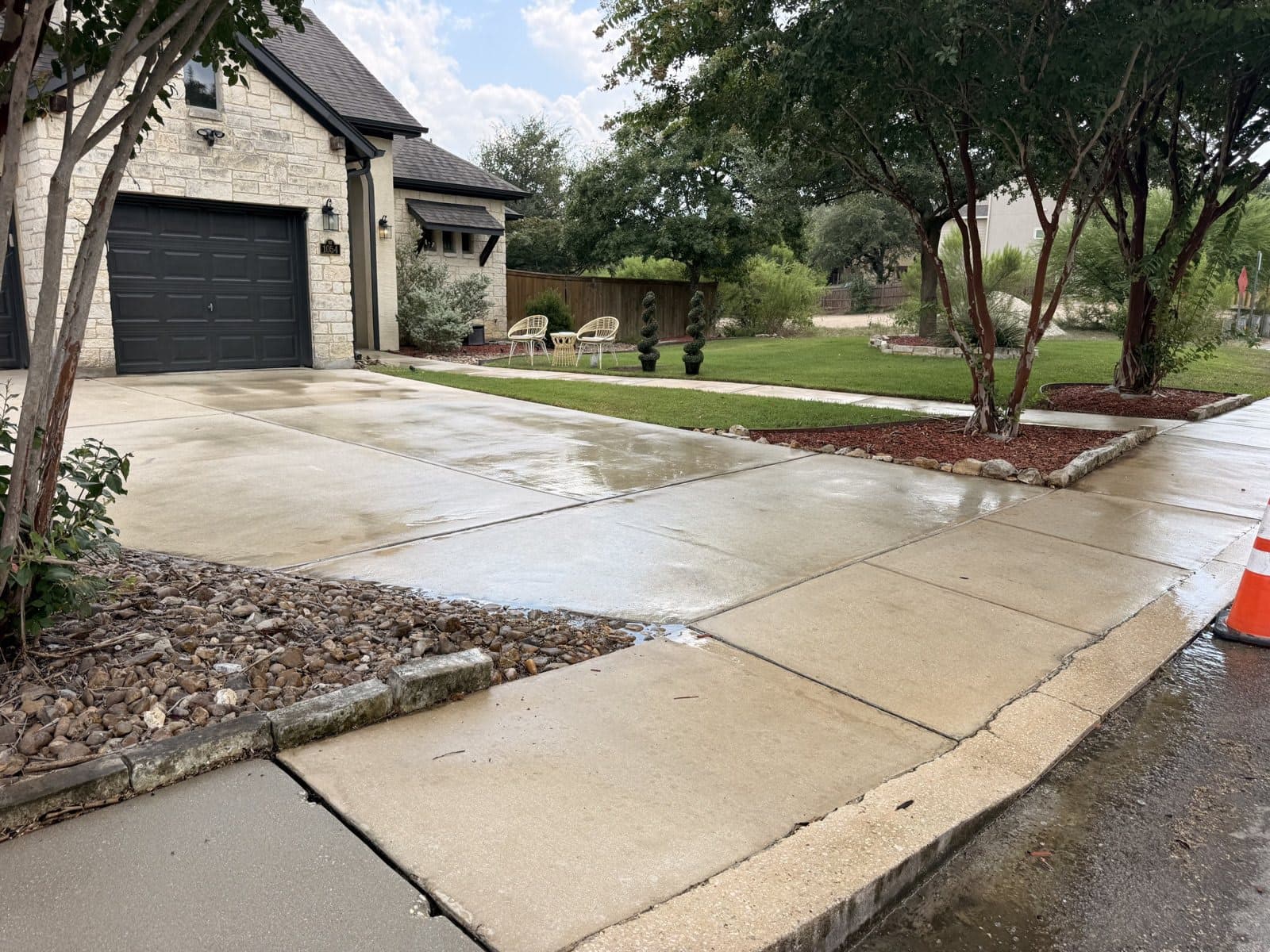 Stone house with its driveway after pressure washing, concrete restored to an even light gray